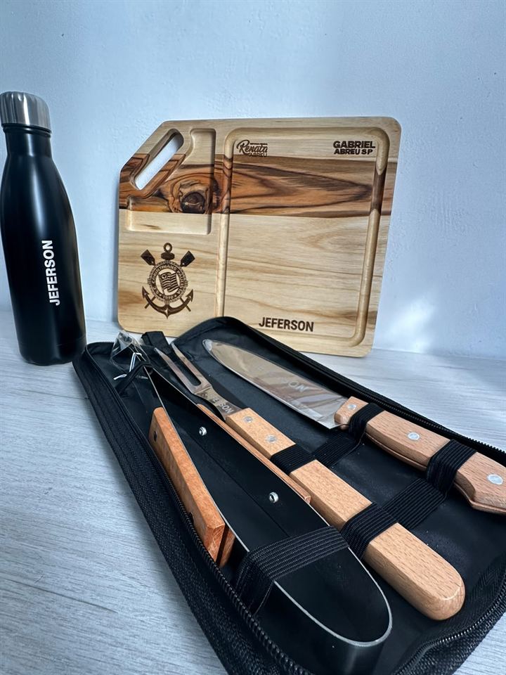 Tábua de churrasco em madeira gravada a laser com nome e escudo de time, ao lado de kit de facas e garrafa personalizada.