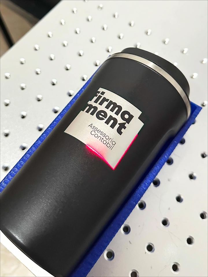 Garrafa térmica preta com logo de empresa sendo gravado a laser na mesa da máquina.