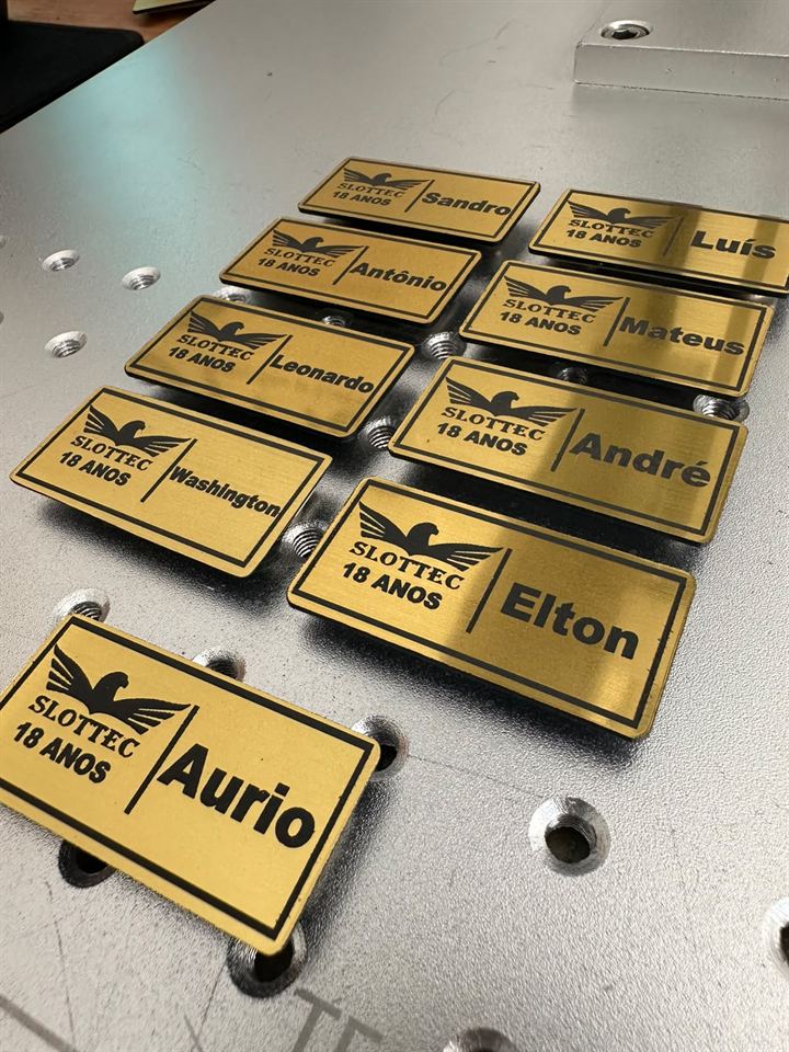 Placas metálicas douradas gravadas a laser com o logo da empresa e o nome de cada colaborador.