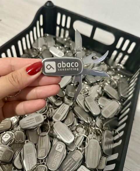 Caixa cheia de chaveiros canivete em metal gravados a laser com logo e QR code.