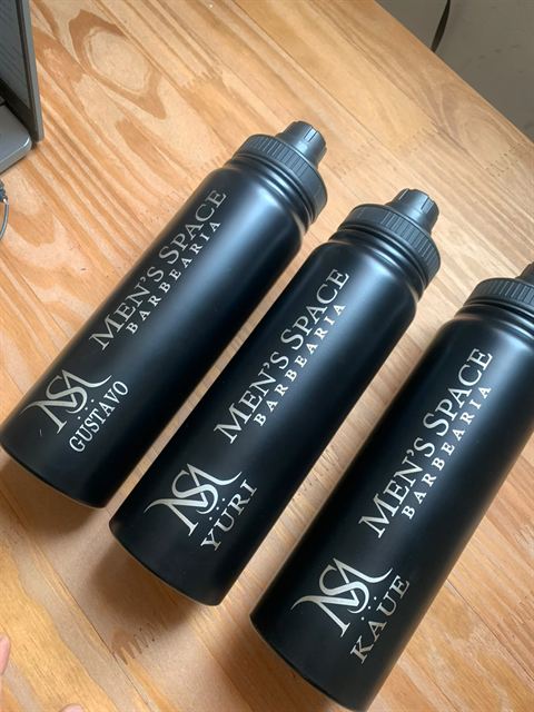 Squeezes pretos gravados a laser com o logo de uma barbearia e o nome de cada profissional.